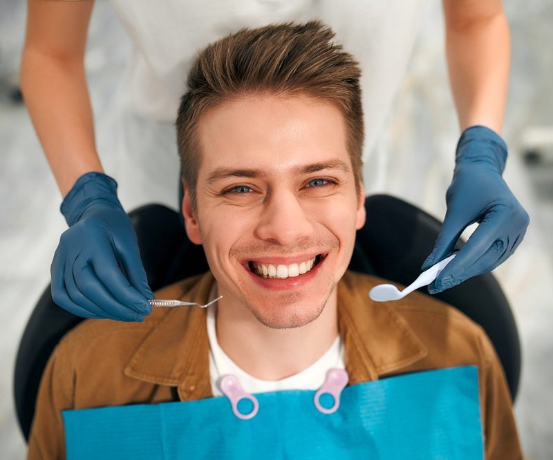 Smiling dental patient during an exam with hygienist tools visible, highlighting care options for those allergic to fluoride - allergic to fluoride