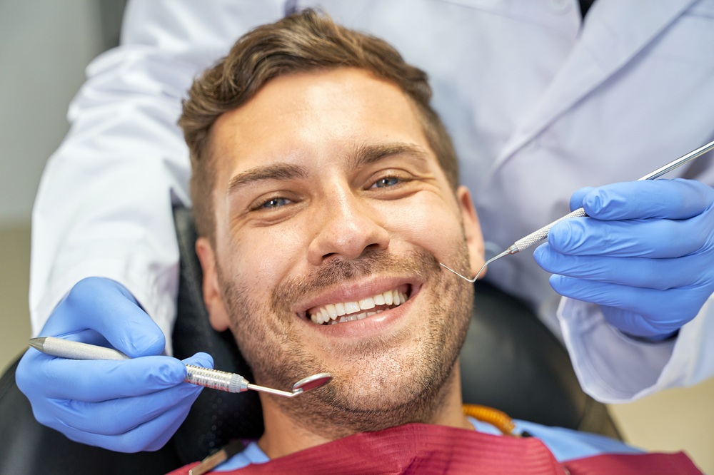 Patient smiling while a dentist smooths and reshapes teeth during a cosmetic procedure – tooth recontouring